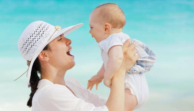 ビーチで母親に抱きあげられる笑顔の赤ちゃん