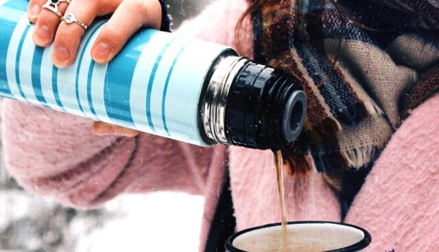 雪の中で水筒から温かい紅茶を注ぐ女性